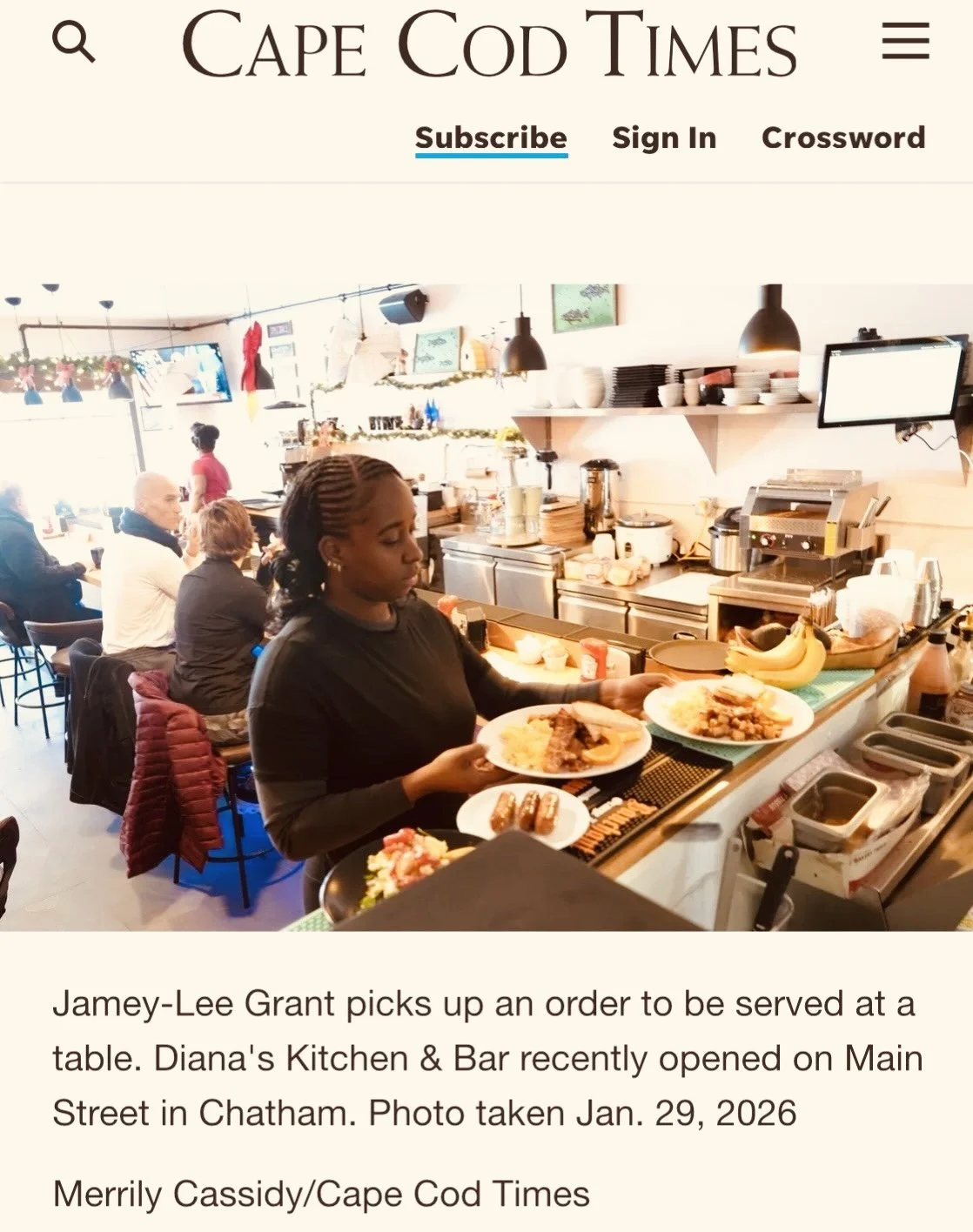 A woman serving food at a counter in a cafe with several customers seated at tables in the background.