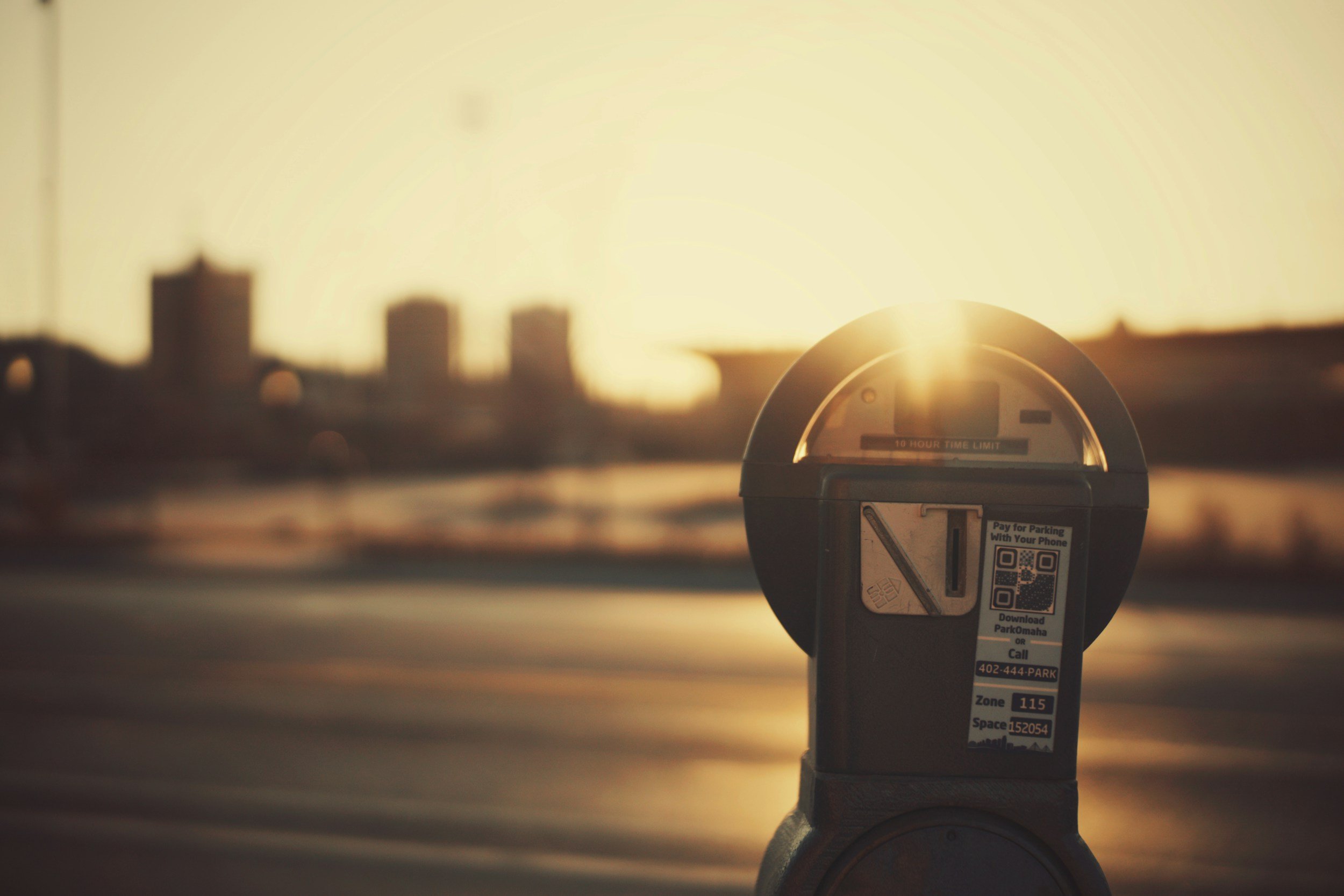 Close-up of a parking meter with a city skyline silhouette in the background during sunset.