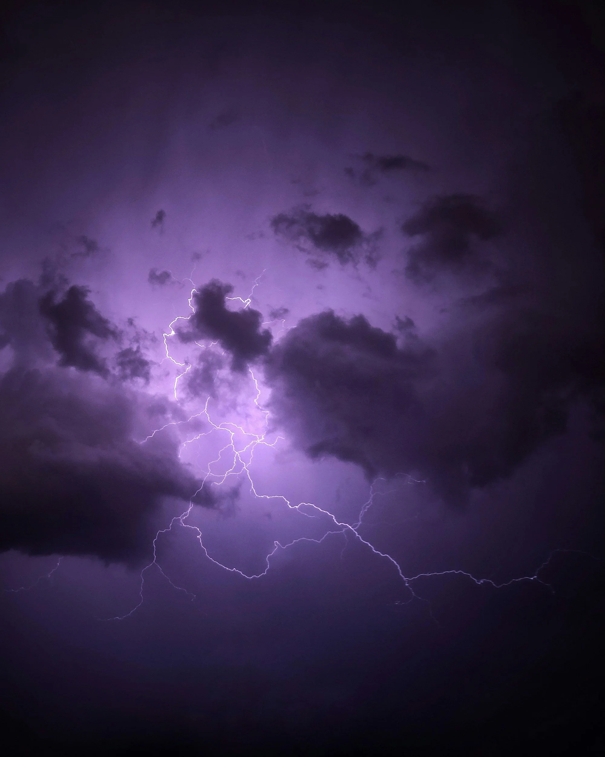 Dark sky filled with dark clouds and visible lightning strikes with purple hues.