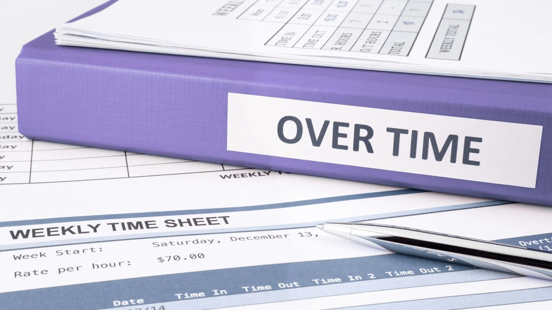 Office files and overtime records stacked on a workspace desk.
