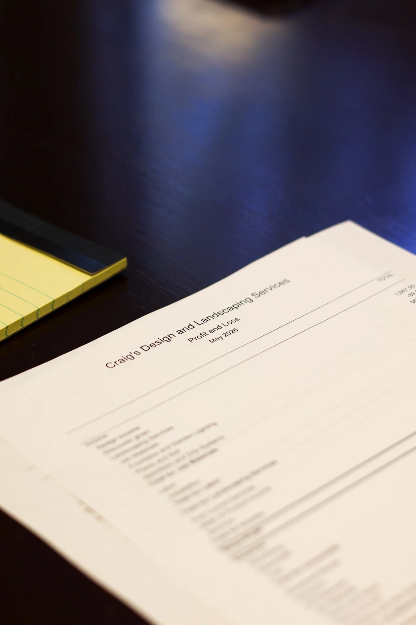 A printed report titled 'Craig's Design and Landscaping Services' on a black surface, with yellow sticky notes partially visible to the left.