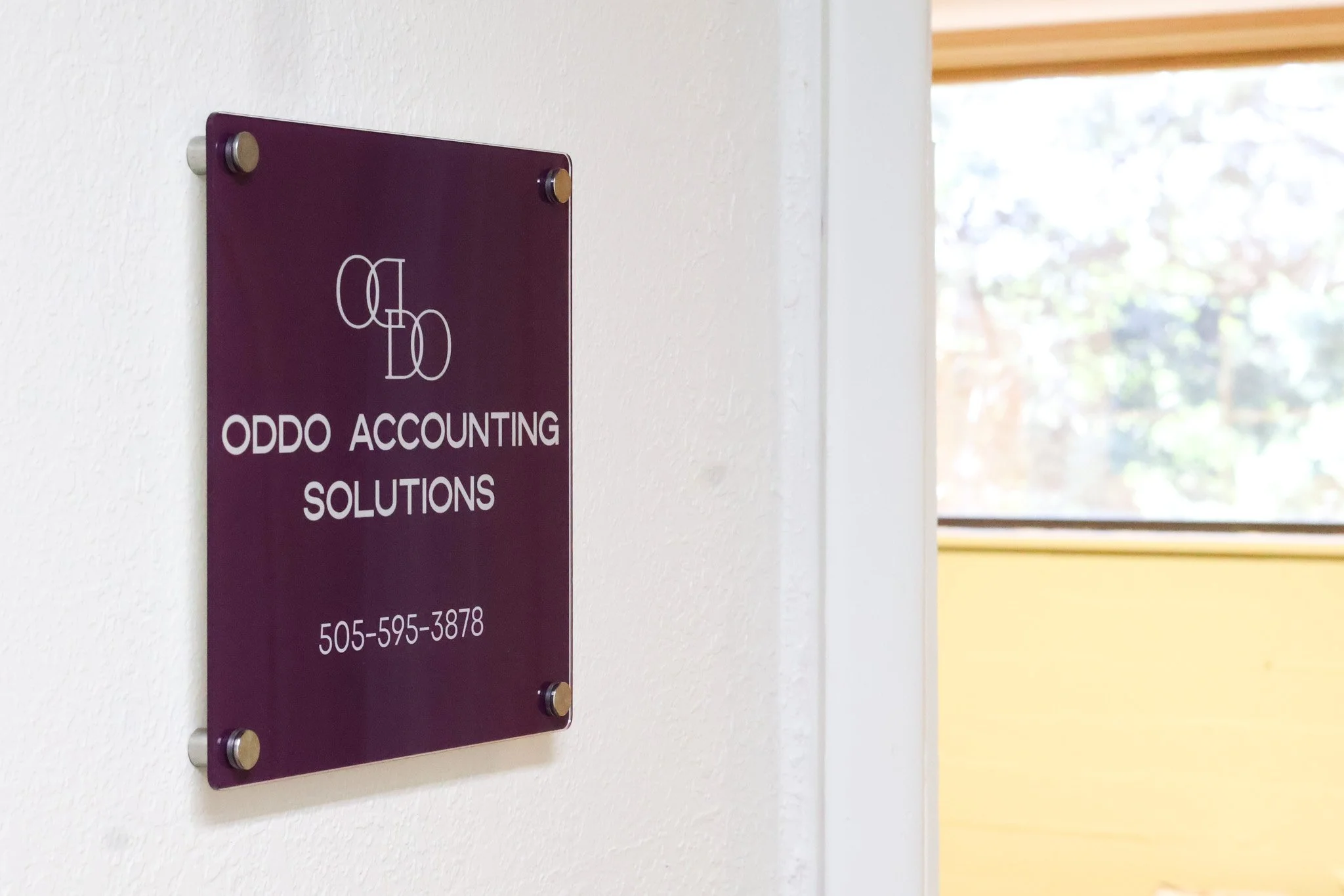 Purple business sign mounted on a white wall, visible near a window with light coming through.