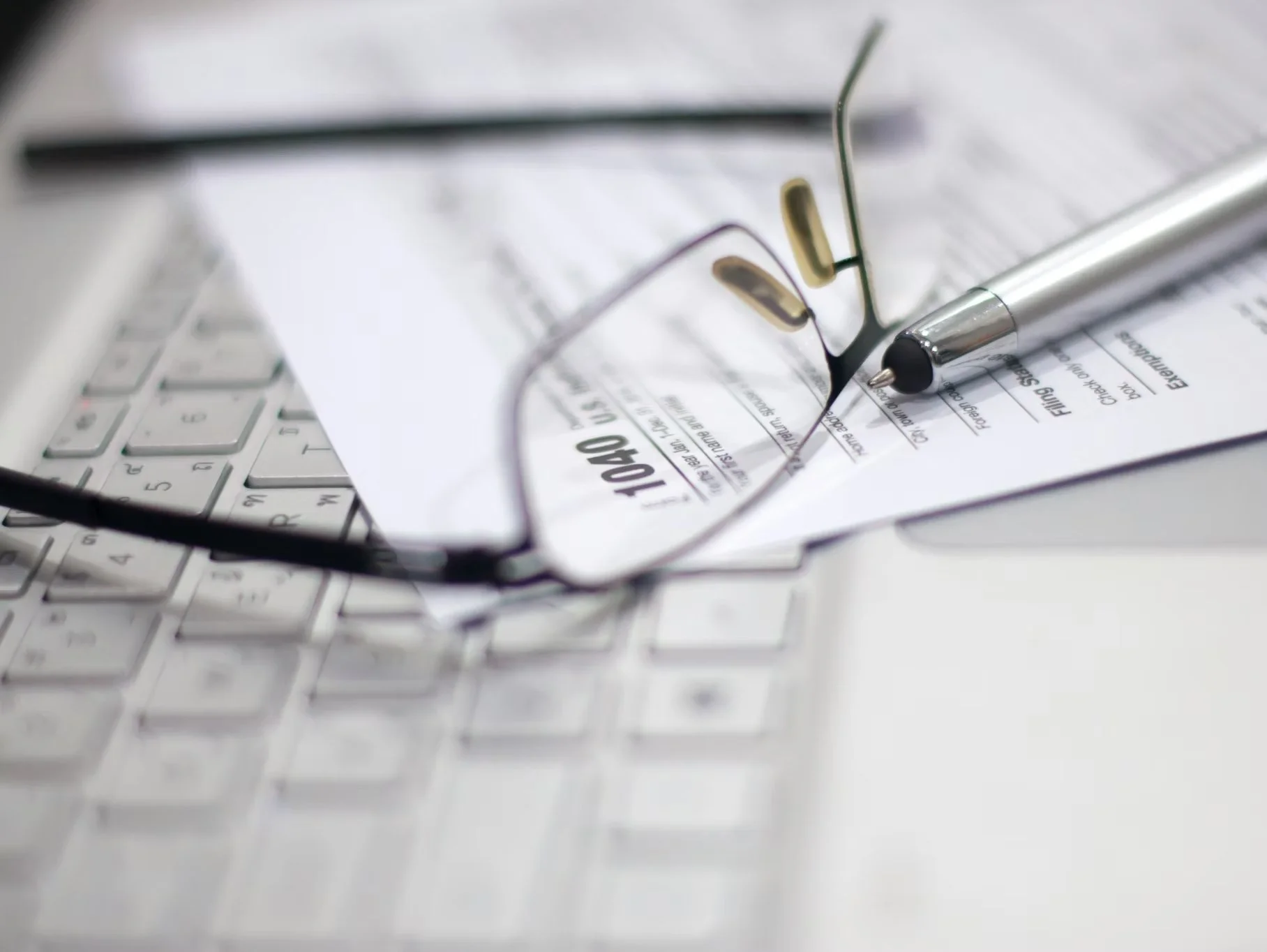 IRS 1040 tax form placed on top of a laptop beside a pair of eyeglasses.