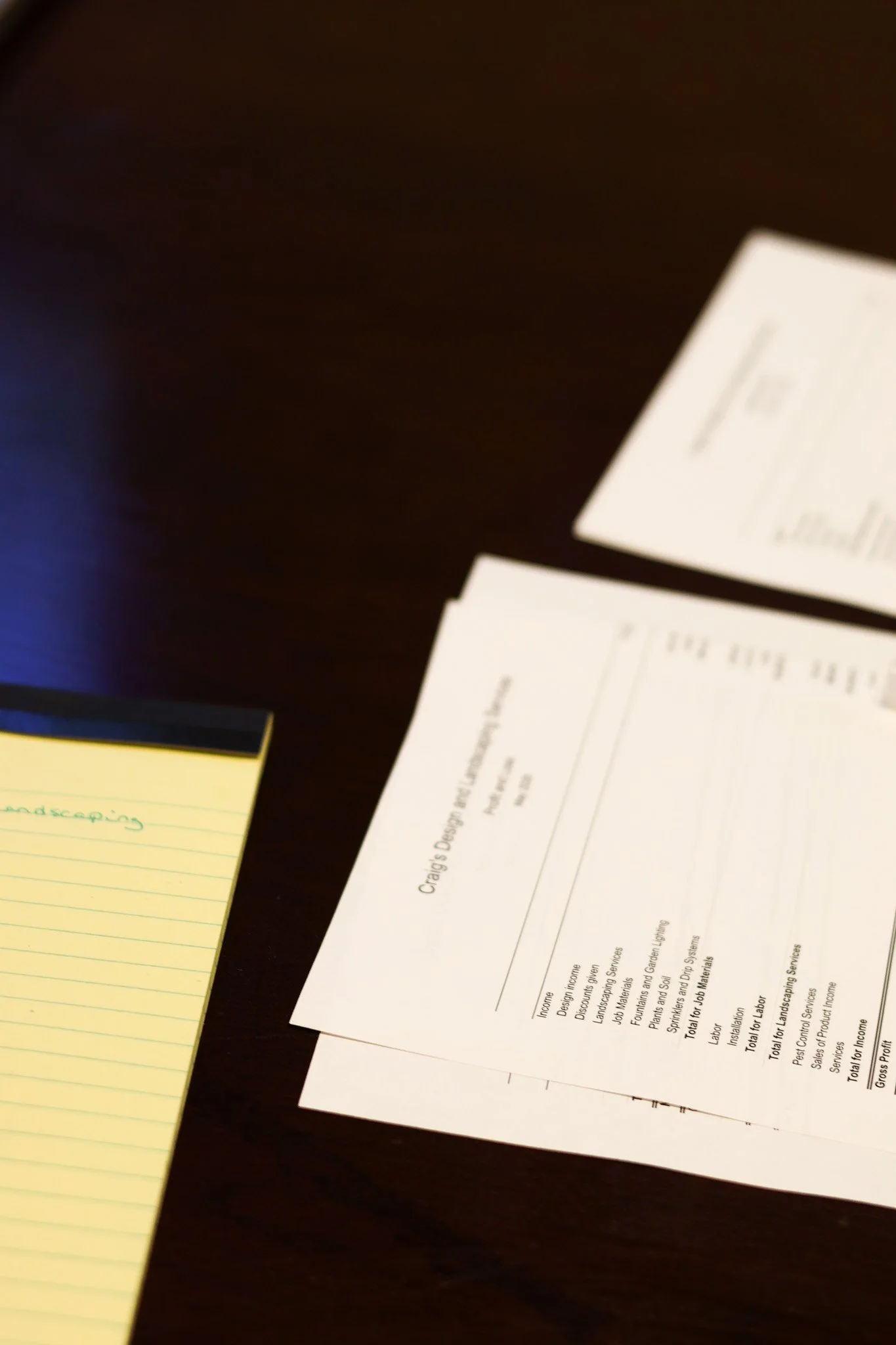 A dark table with a yellow sticky note and several printed documents.
