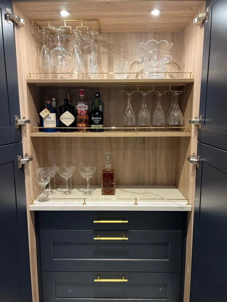 A built-in wooden cabinet with glassware and liquor bottles displayed on its shelves and a marble countertop.