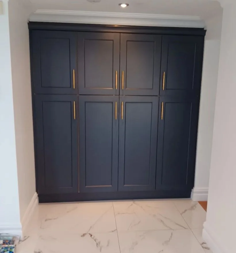 Dark blue built-in cabinet with gold handles in a room with white marble floor and white walls.