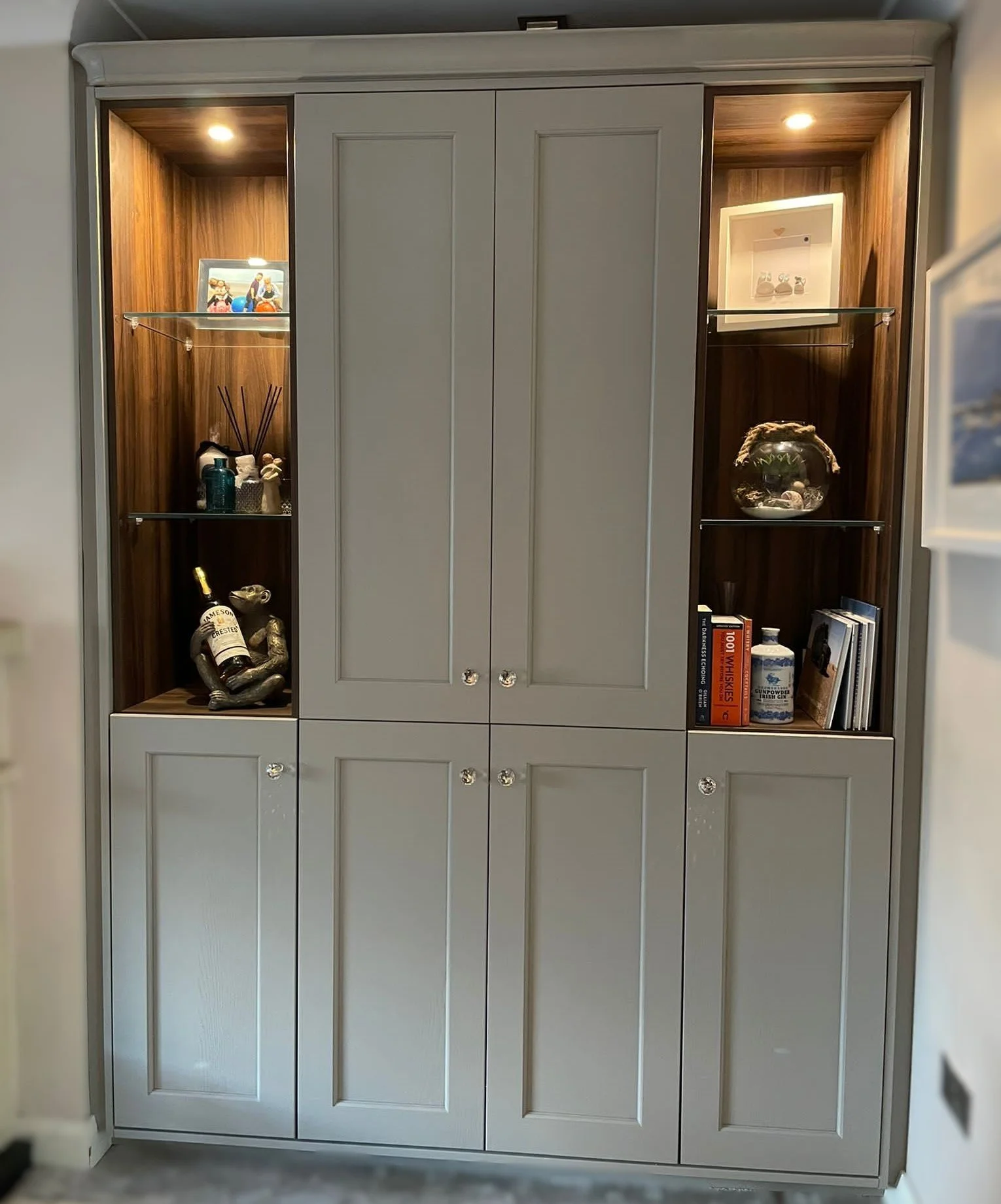 A built-in cabinet with closed doors, featuring decorative knobs and glass display sections illuminated from within, filled with various decorative items, books, and small collectibles.