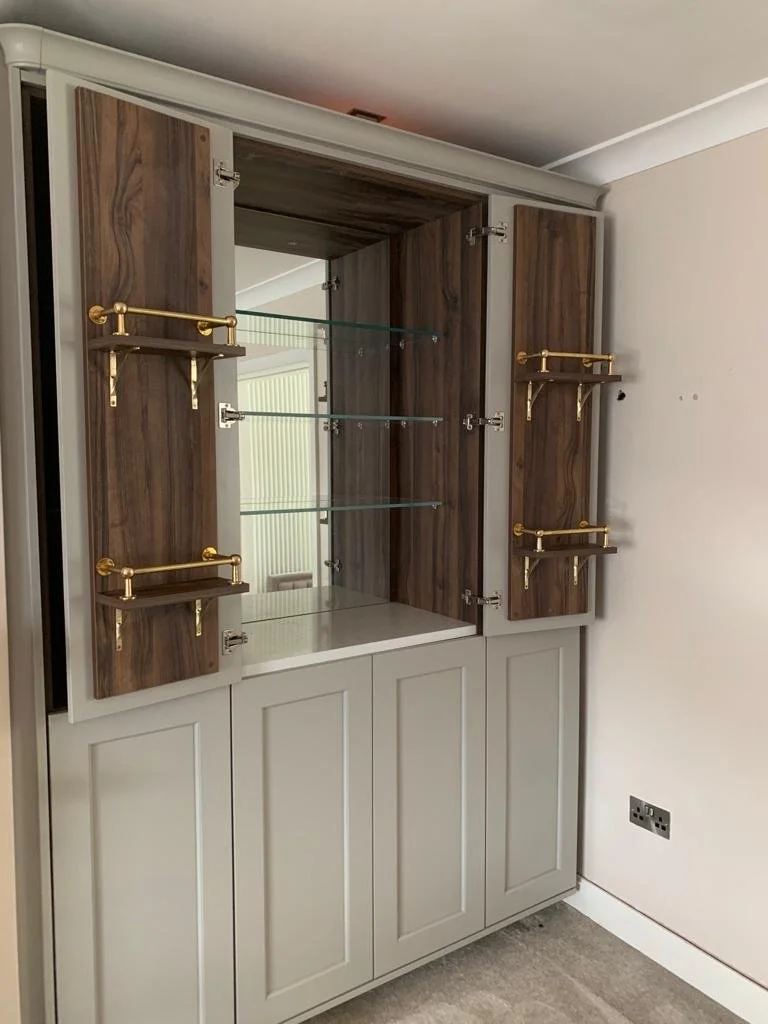 A built-in cabinet with gray lower panels, wooden upper doors, and glass shelves inside. Gold brackets are mounted on the wooden doors for additional storage.