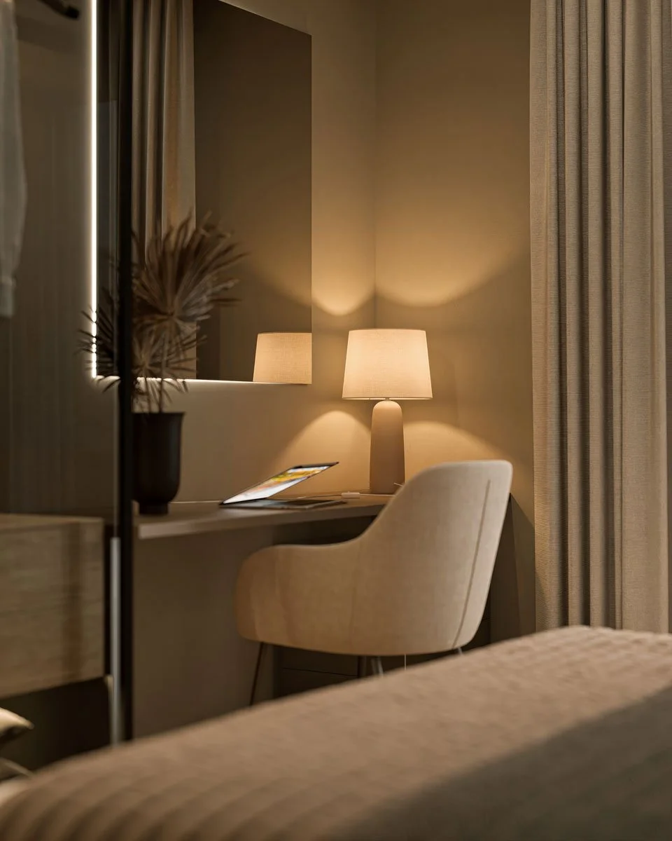 Angolo di una camera da letto con scrivania, sedia morbida, lampada da tavolo accesa, specchio e tende beige.