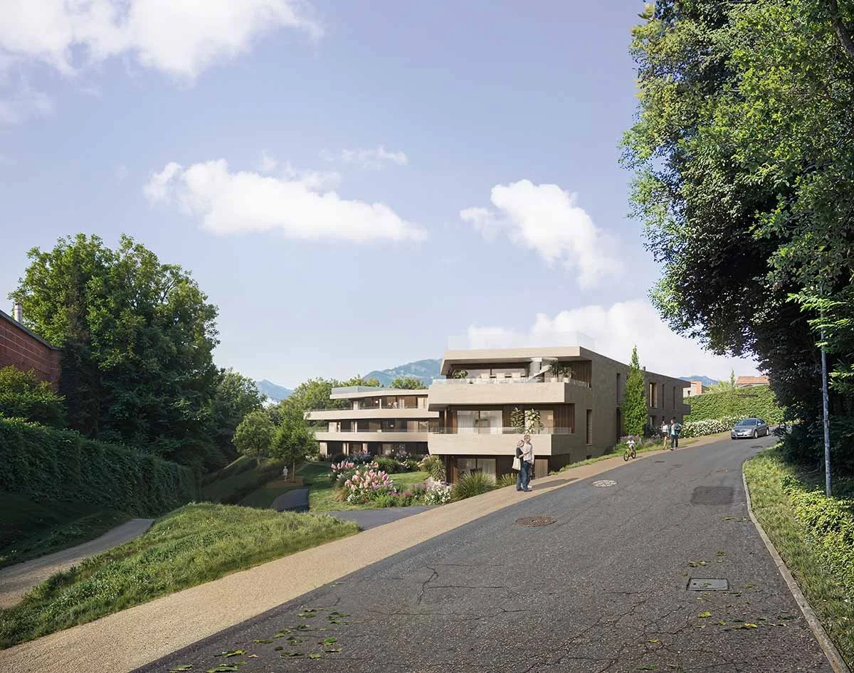 Immagine di un complesso residenziale moderno con più edifici, circondato da natura, su una strada leggermente in pendenza, con alcune persone e automobili visibili, e un cielo soleggiato con alcune nuvole.