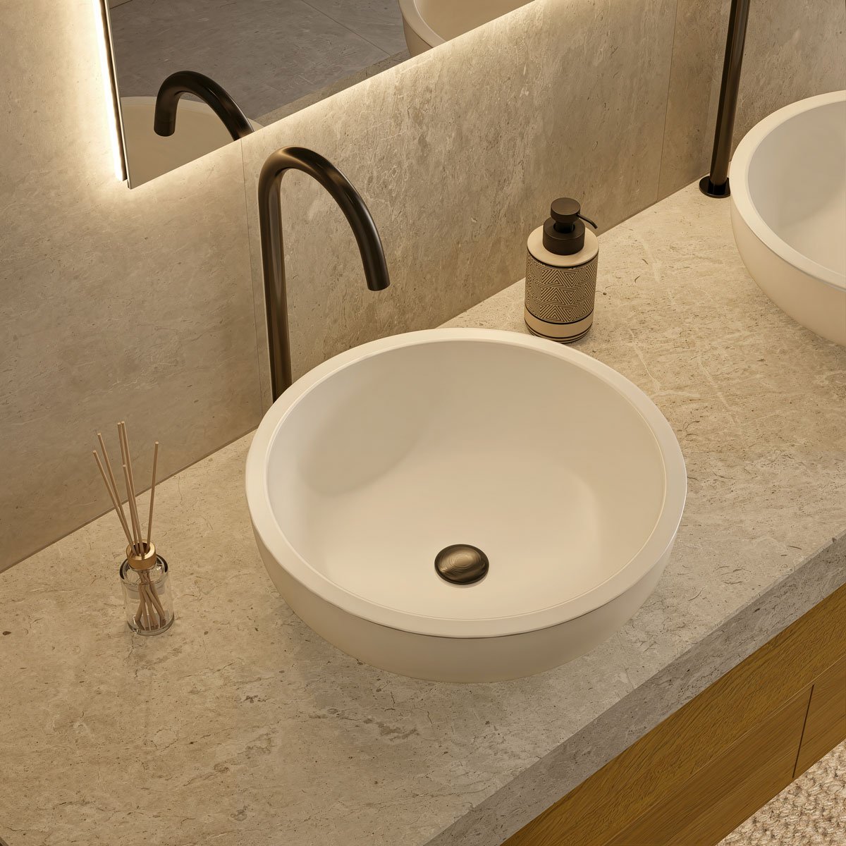 Lavandino rotondo bianco con manico nero, specchio, sapone in dispenser decorativo, e diffusore di profumo in vetro con bastoncini di rattan, in un bagno moderno.