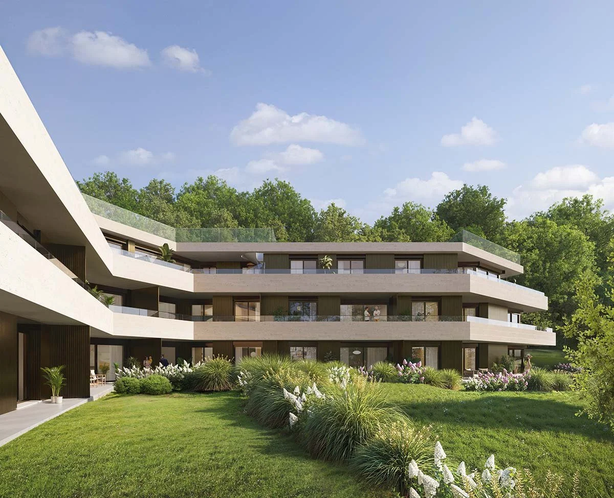 Edificio residenziale moderno circondato da giardino verde con piante e fiori, con una collina di alberi sullo sfondo e un cielo azzurro con alcune nuvole.