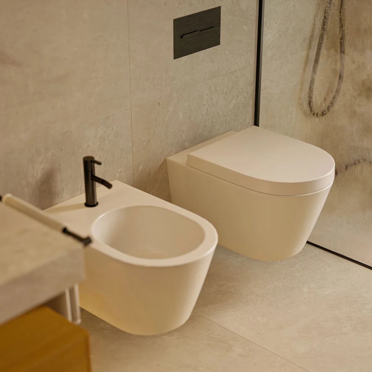 Bagno moderno con WC sospeso e bidet, rivestimenti in pietra beige.