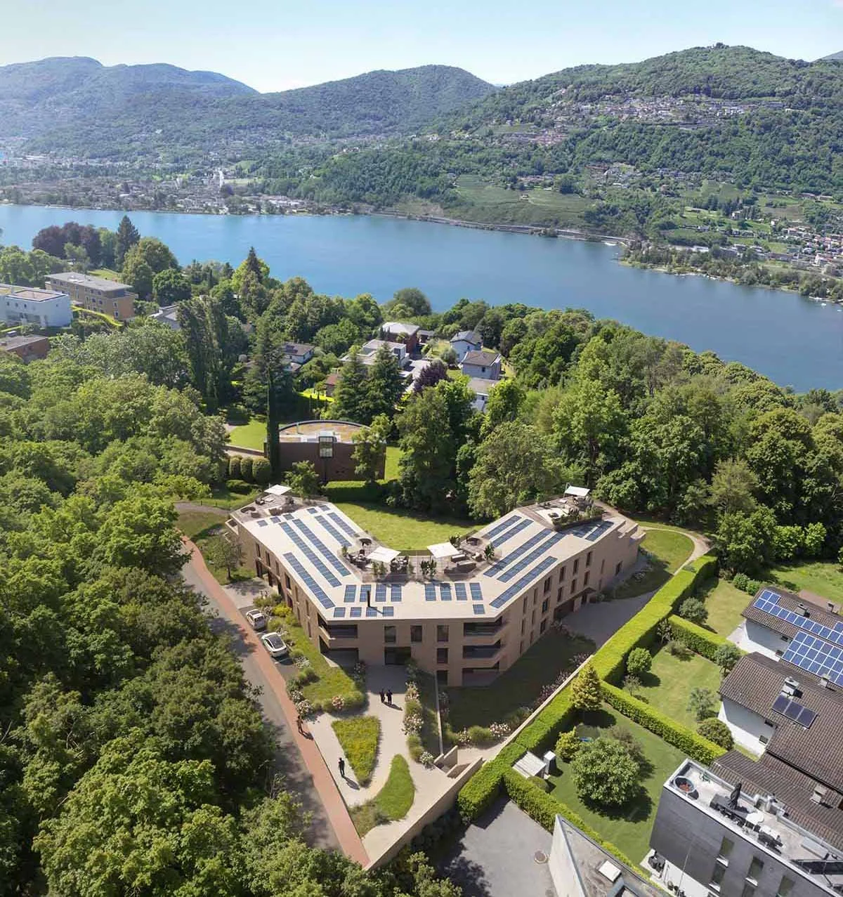 Veduta aerea di una zona residenziale vicino a un lago circondata da colline verdi e montagne.