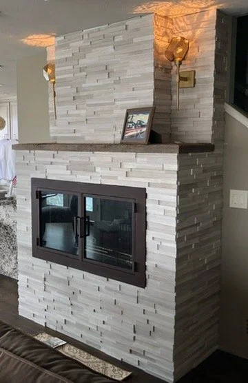“This custom fireplace features a veneer stone surround, a wood mantel, two modern lights above, and new designer doors, creating a contemporary and inviting focal point for the room.”