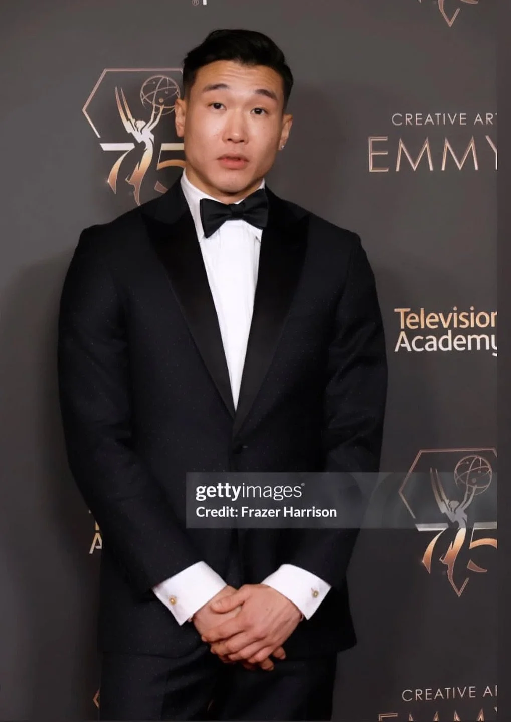 Man in black tuxedo with bowtie standing against a backdrop with Emmy Award logo, Televison Academy, and Creative Arts Emmy text.