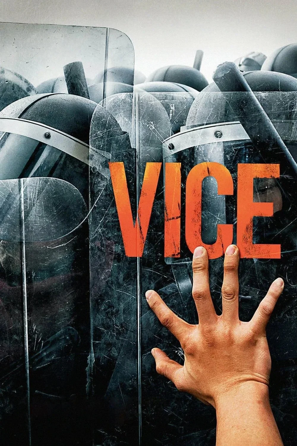 A human hand pressing a police riot shield with the word 'VICE' written in large orange letters. Behind the shield, multiple police helmets are visible.
