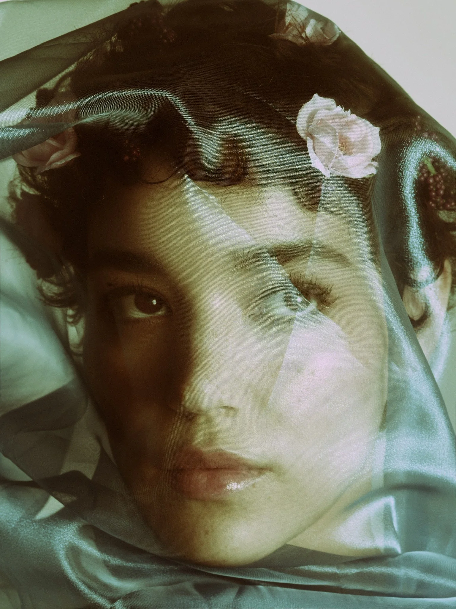 Close-up of a woman's face on a fabric, with visible eyes, nose, and lips, adorned with a black veil and pink flower decorations.