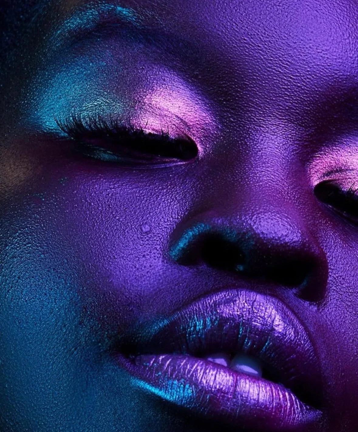 Close-up of a person's face illuminated with purple, blue, and pink neon lights, highlighting smooth skin and features.