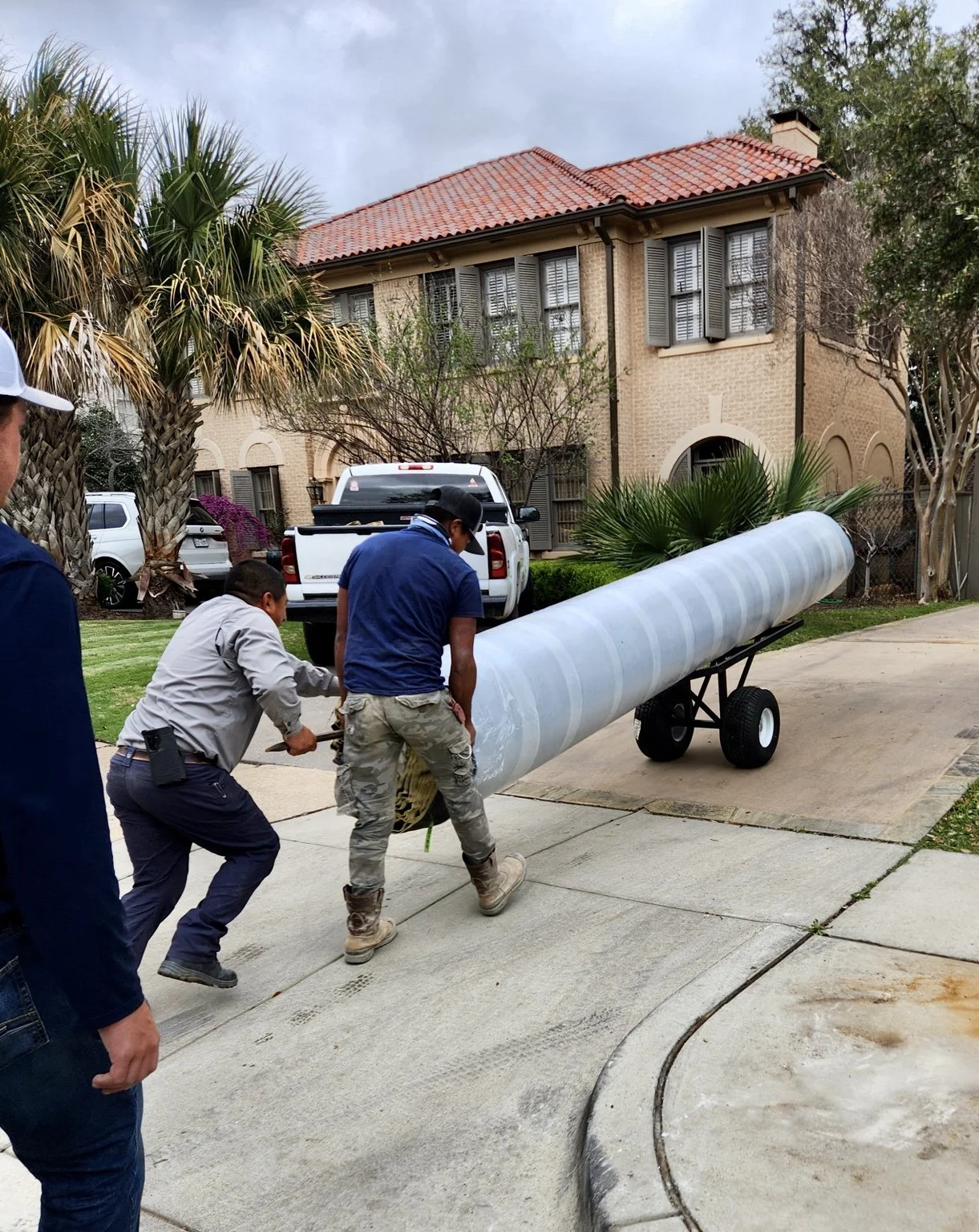 Workers guide a large roll of carpet on the Carpet Dolly up a residential driveway.
