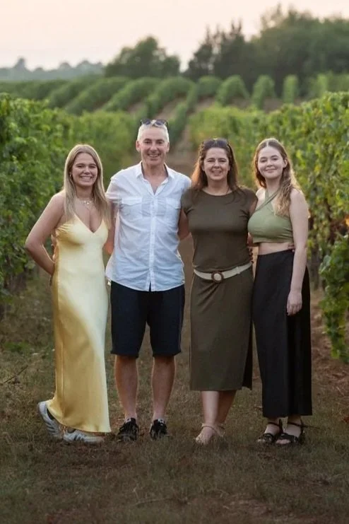 Four people standing together in a vineyard during sunset, smiling at the camera.