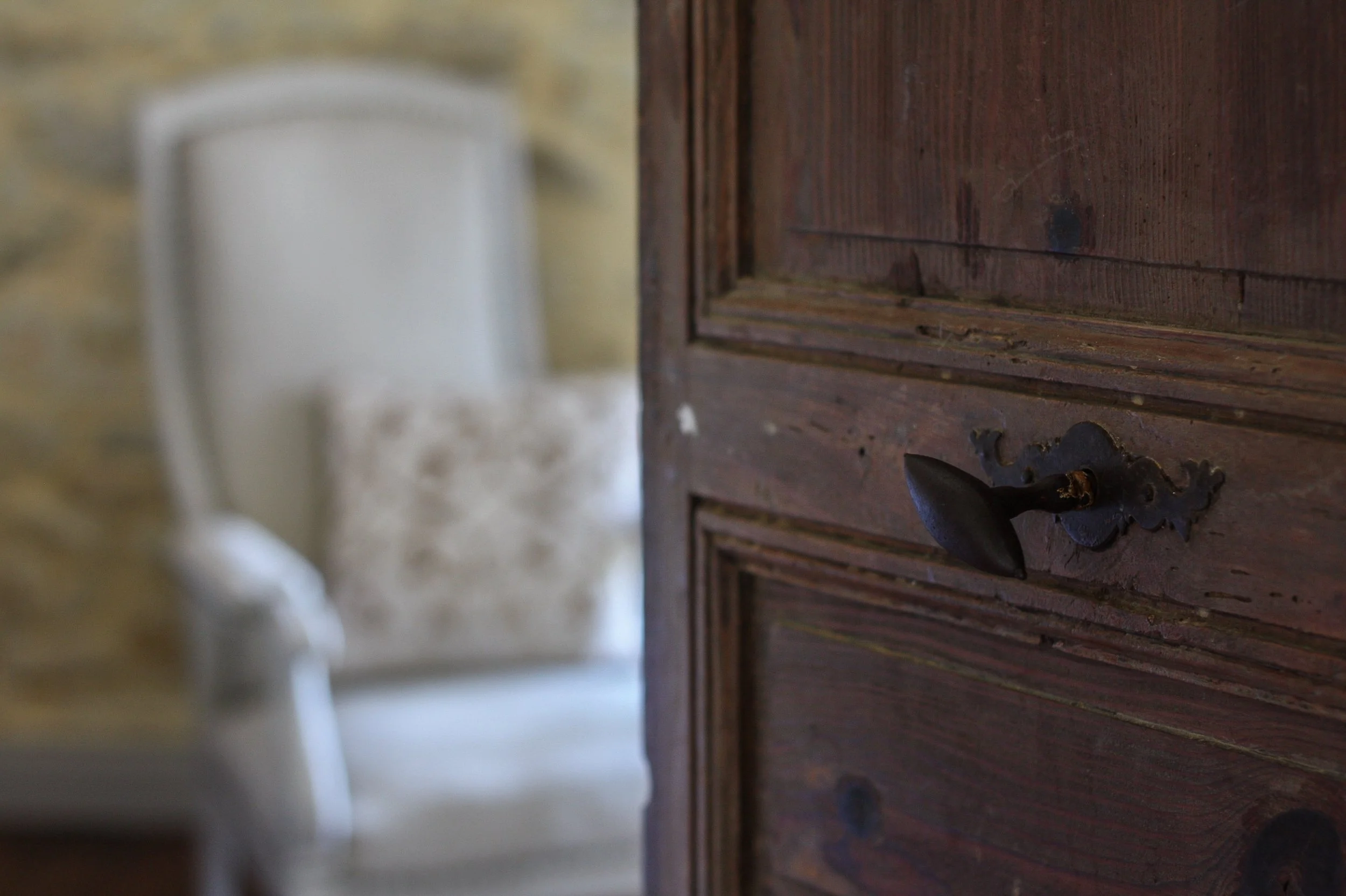 Close-up of a dark brown wooden door with an antique black iron latch, viewed from the side with a blurred background.