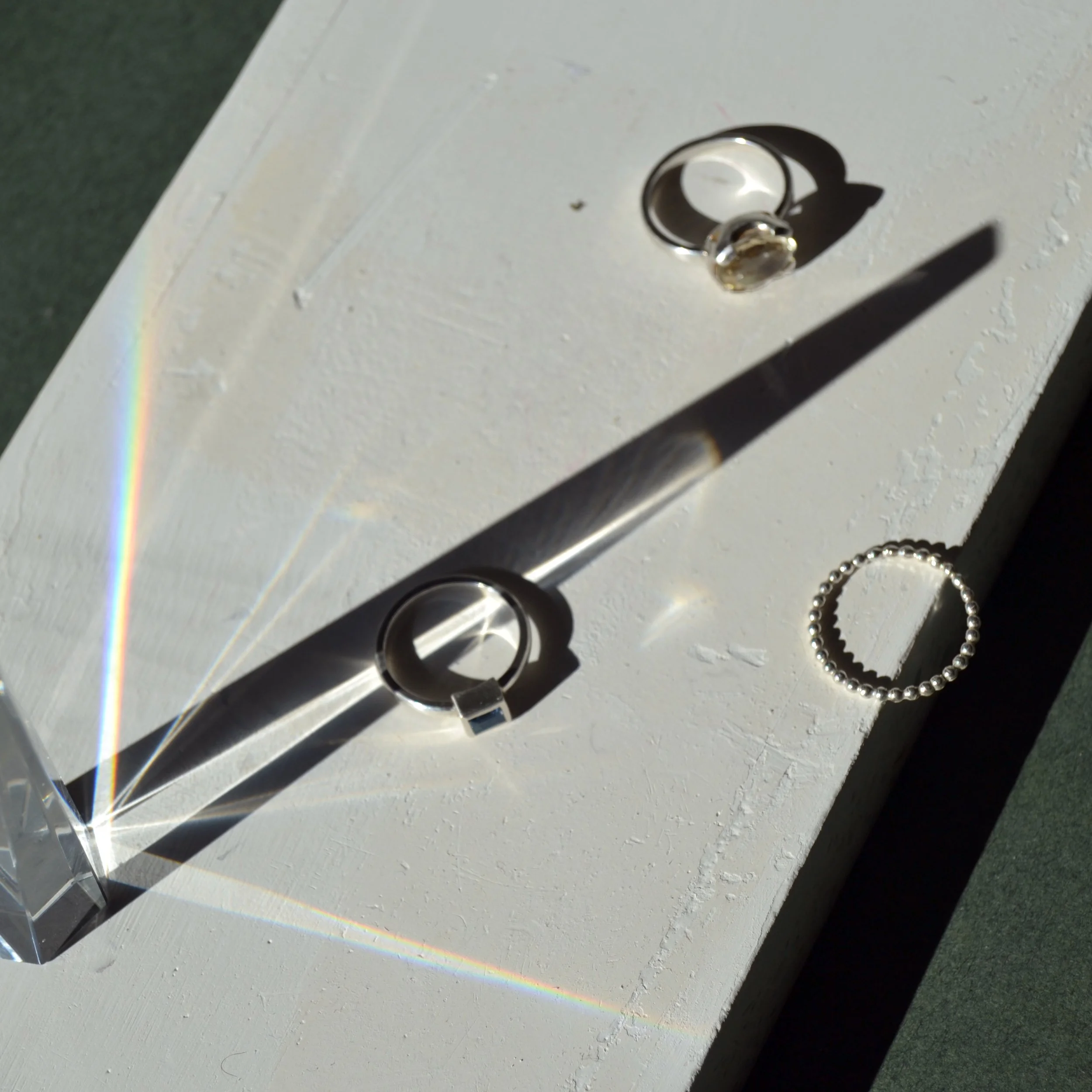 Imagen de una caja blanca con un pomo de puerta de metal y una cadena de perlas al lado, con un reflejo prismático en la superficie.