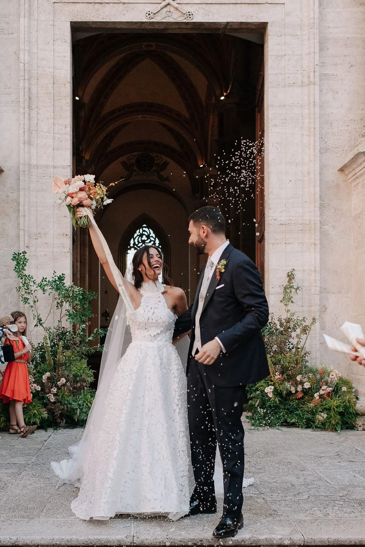 Coppia di sposi che festeggia all'uscita dalla chiesa, con fiori e confetti.