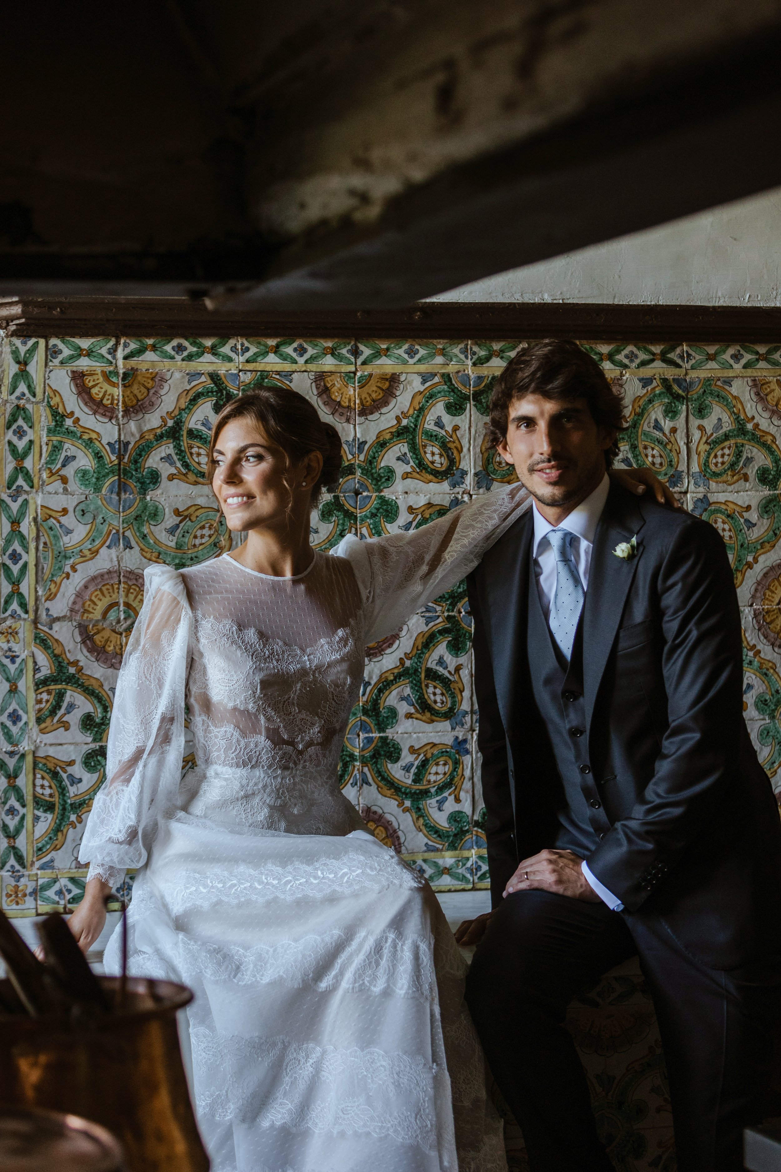 Una coppia di sposi in abiti eleganti, seduti davanti a un mosaico colorato.