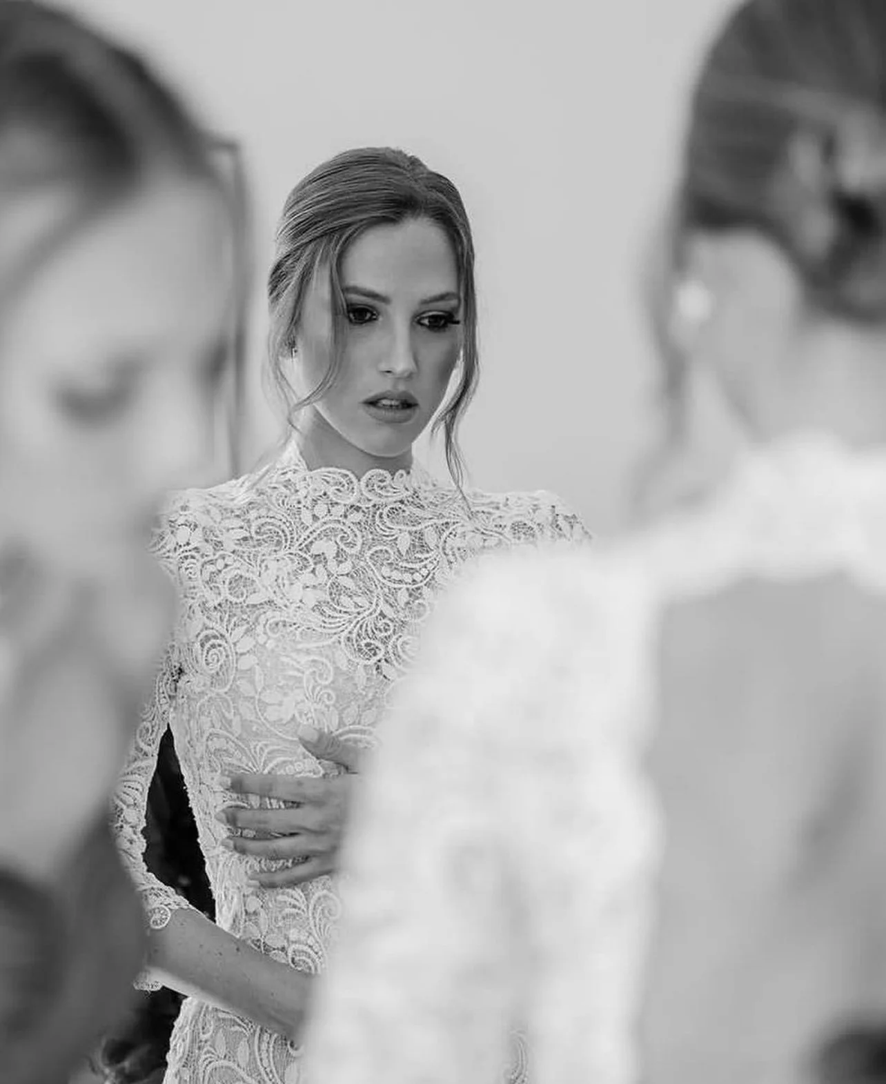 Una donna con abito bianco in pizzo, circondata da altre donne, sembra triste o preoccupata.