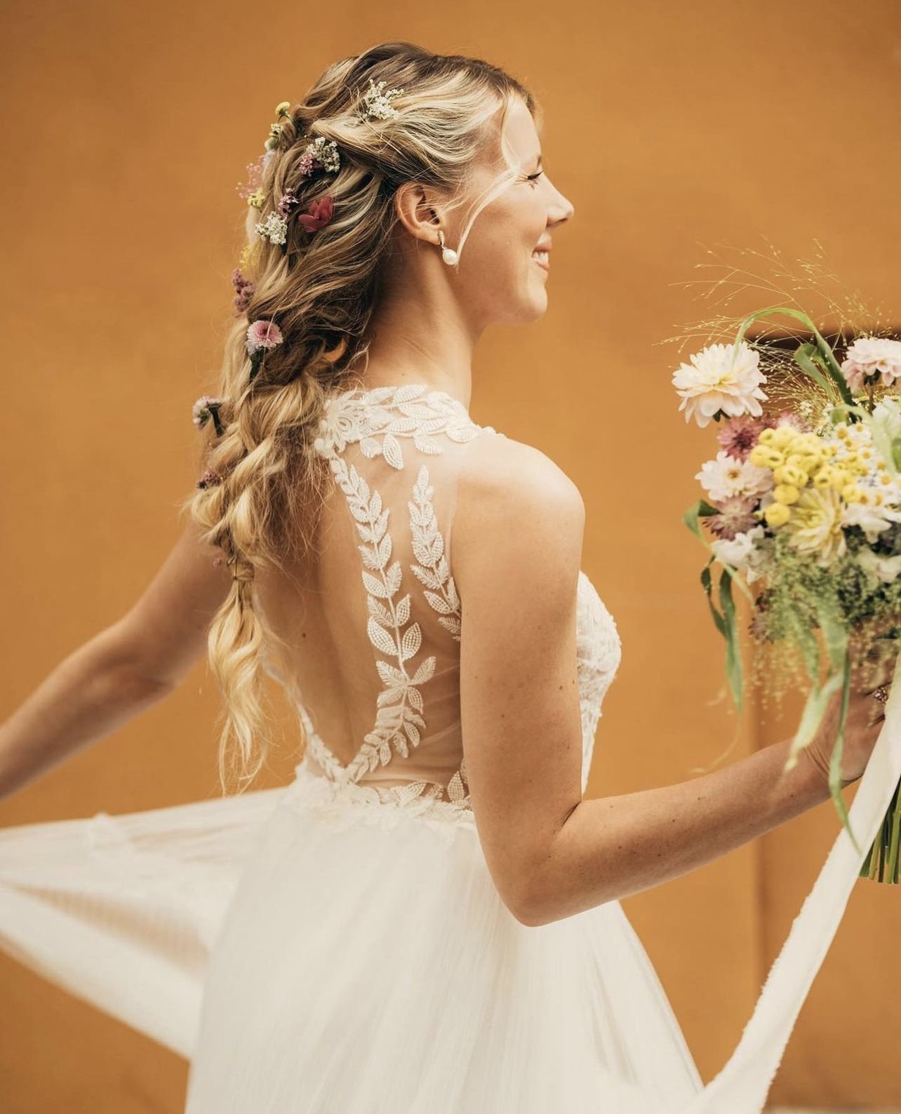 Donna in abito da sposa con capelli decorati con fiori e che sorride mentre tiene un bouquet di fiori colorati.