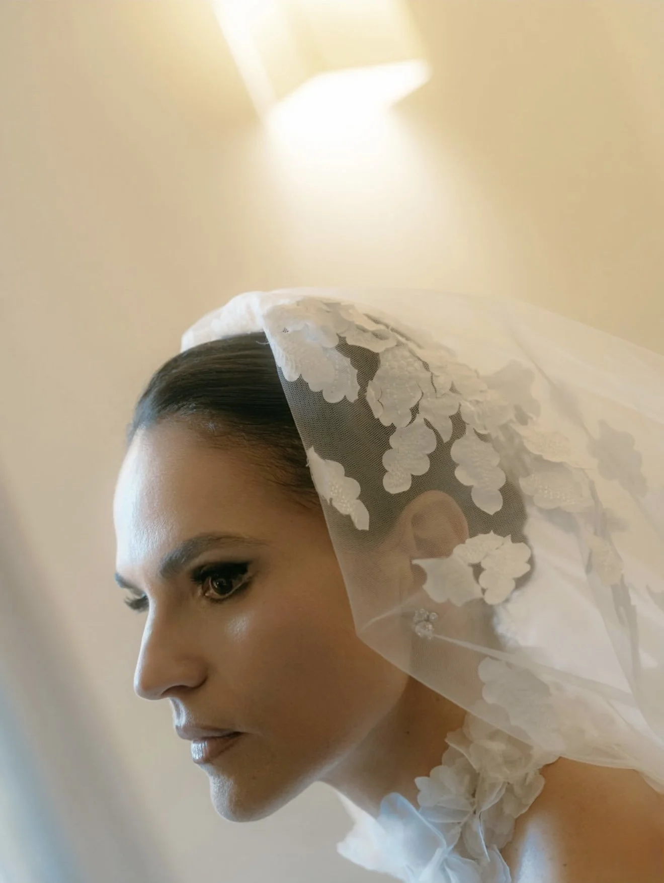 Ragazza con abito da sposa e velo, vista laterale, in un ambiente luminoso.