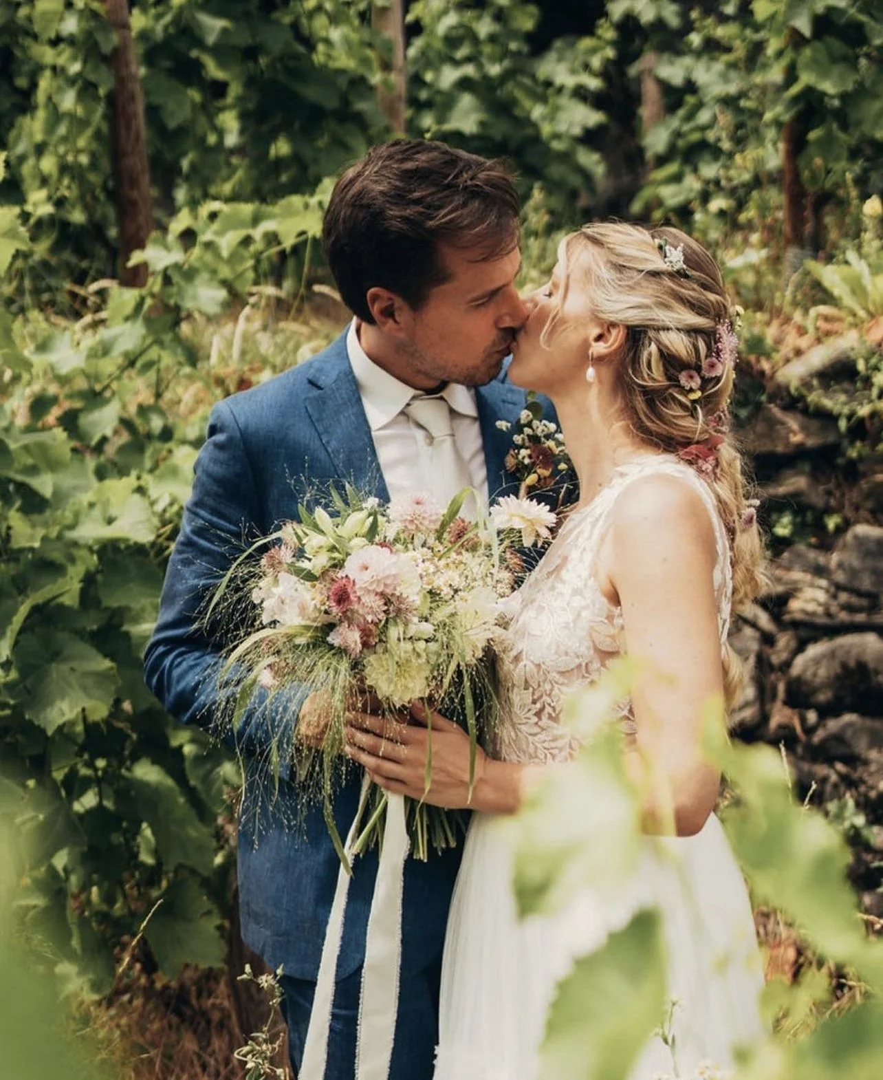 Coppia di sposi che si baciano nel bosco, la donna tiene un bouquet di fiori