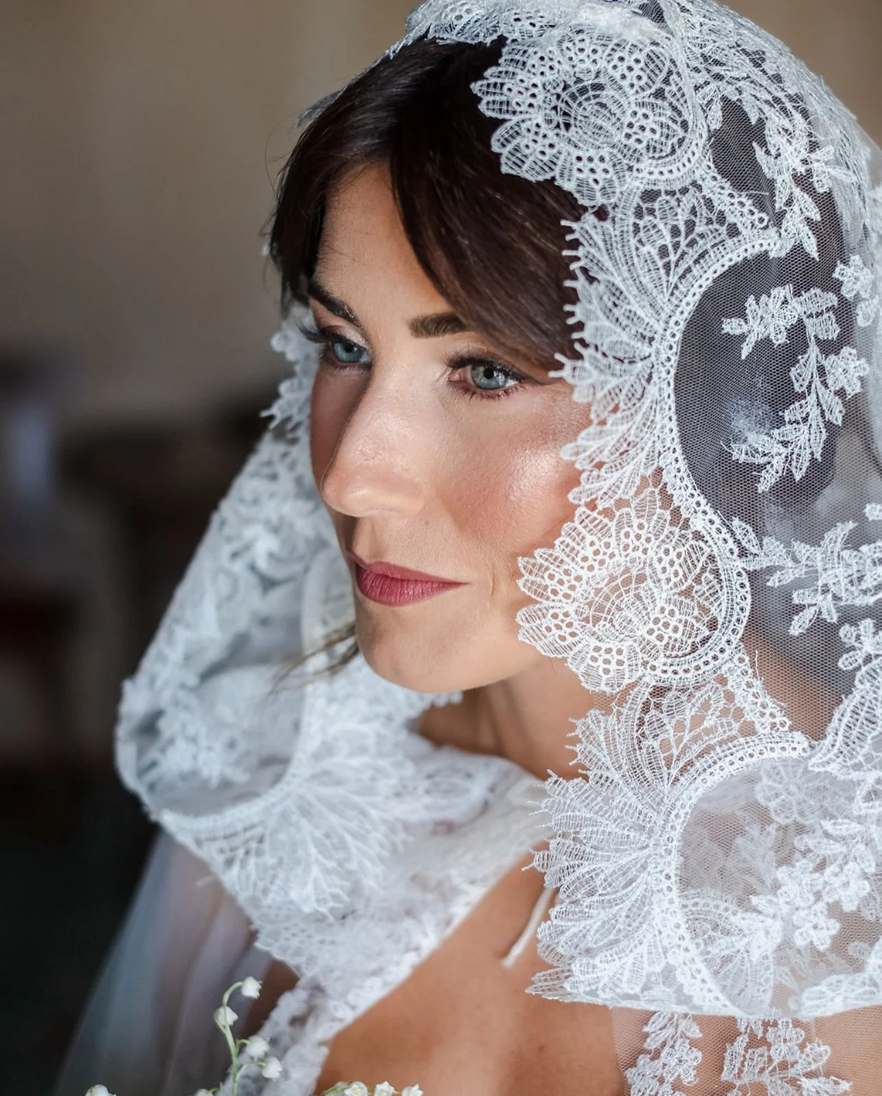 Ragazza con velo bianco di pizzo su capelli castani, occhi azzurri e labbra rosse.