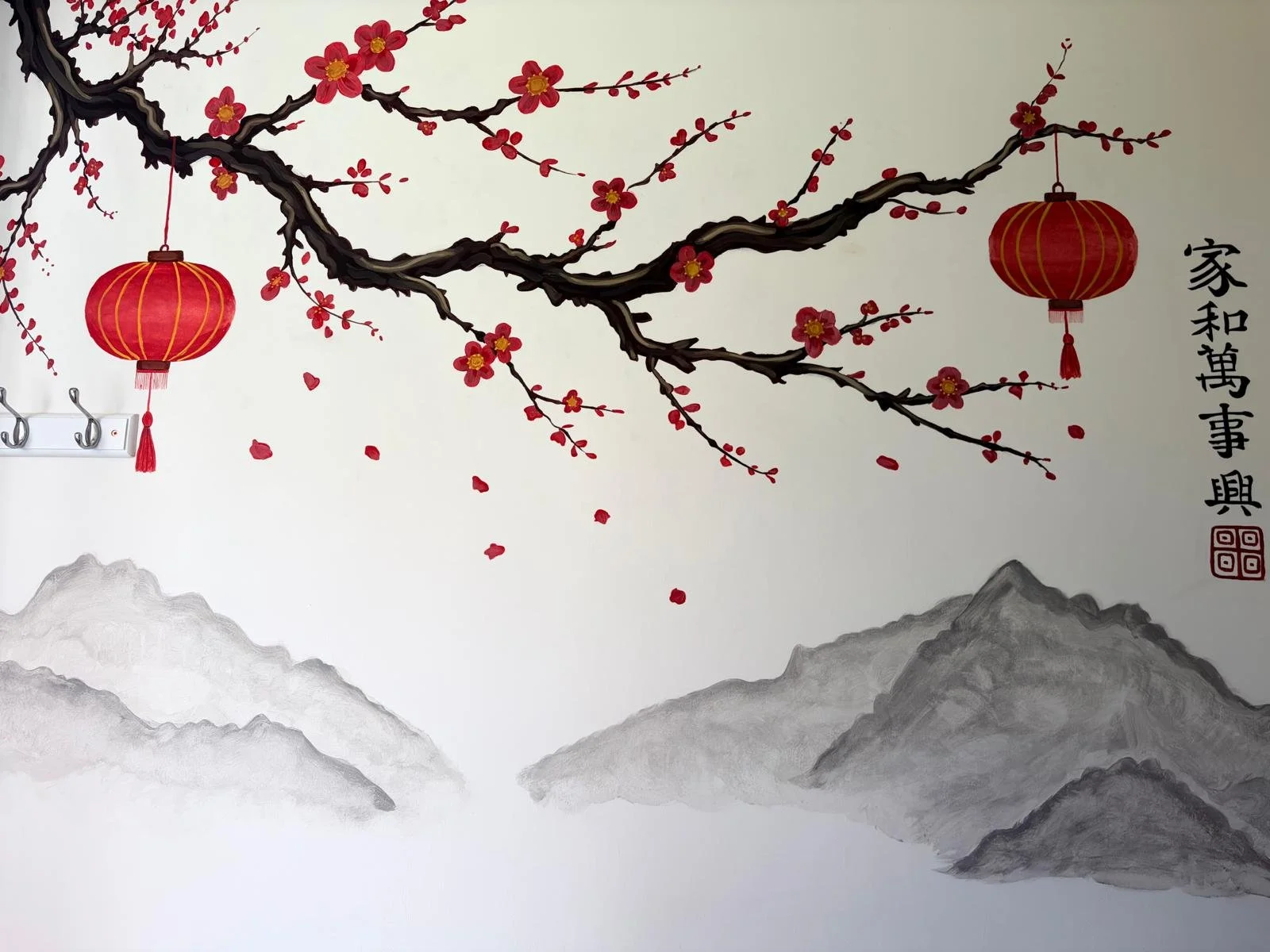 Decorative wall art featuring a cherry blossom branch with pink flowers and red lanterns, gray mountains in the background, and Chinese calligraphy.