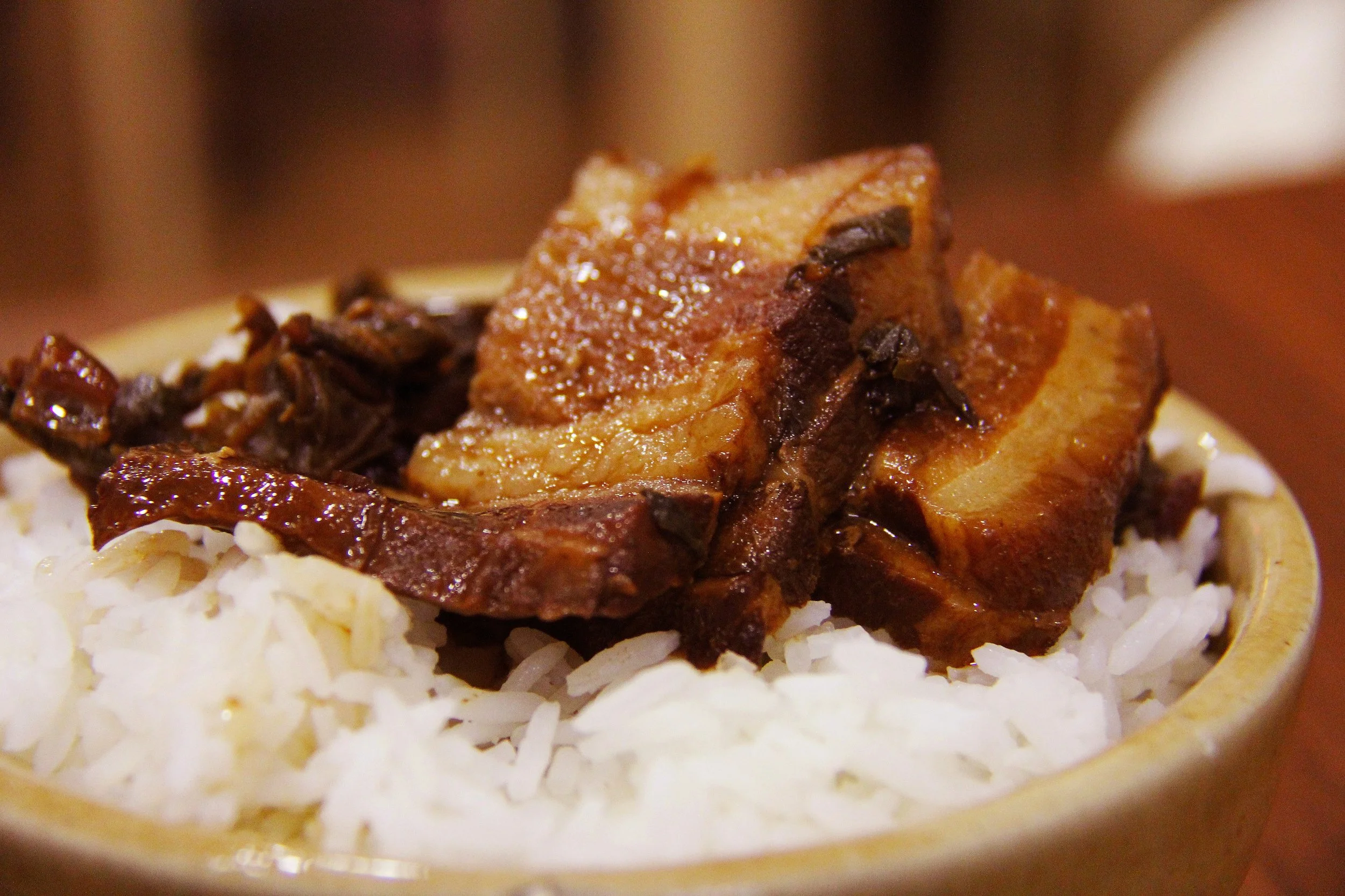 Close-up of cooked pork belly slices on rice with shredded cheese underneath.