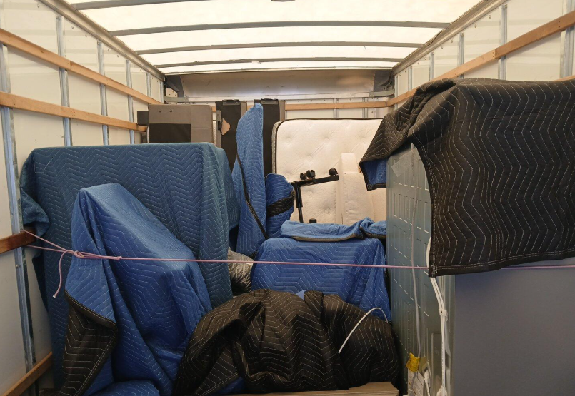 U-Haul truck filled with mattresses and furniture covered with moving blankets, secured with ratchet strap.