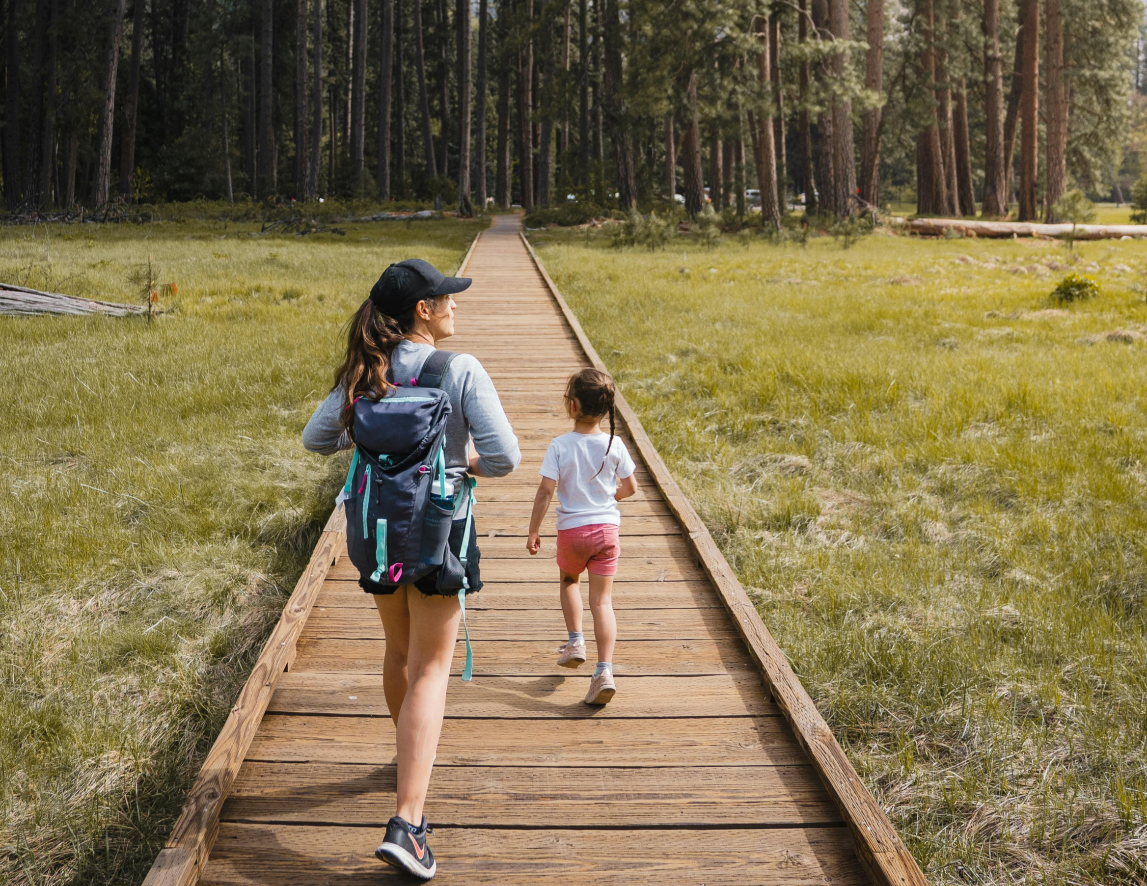 A woman and two children walk along a wooden boardwalk through a grassy forested area.