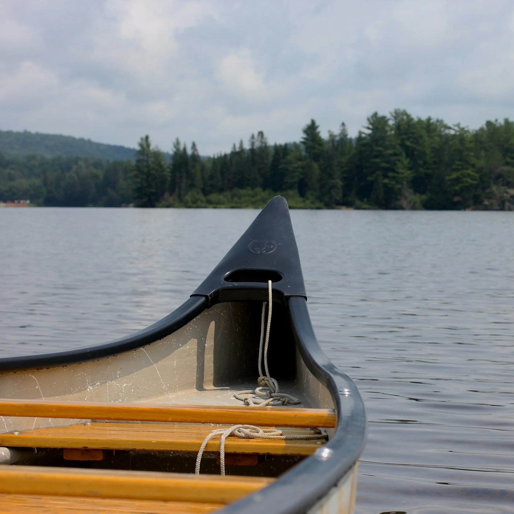 Photo of a canoe on a calm lake with distant trees and a cloudy sky in the background.