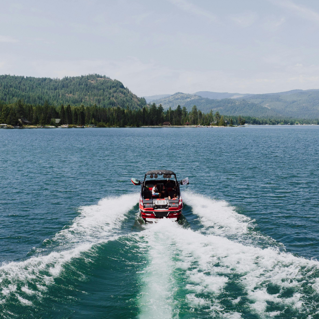 A boat speeding across a lake with a wake behind it, surrounded by mountains and trees in the background.