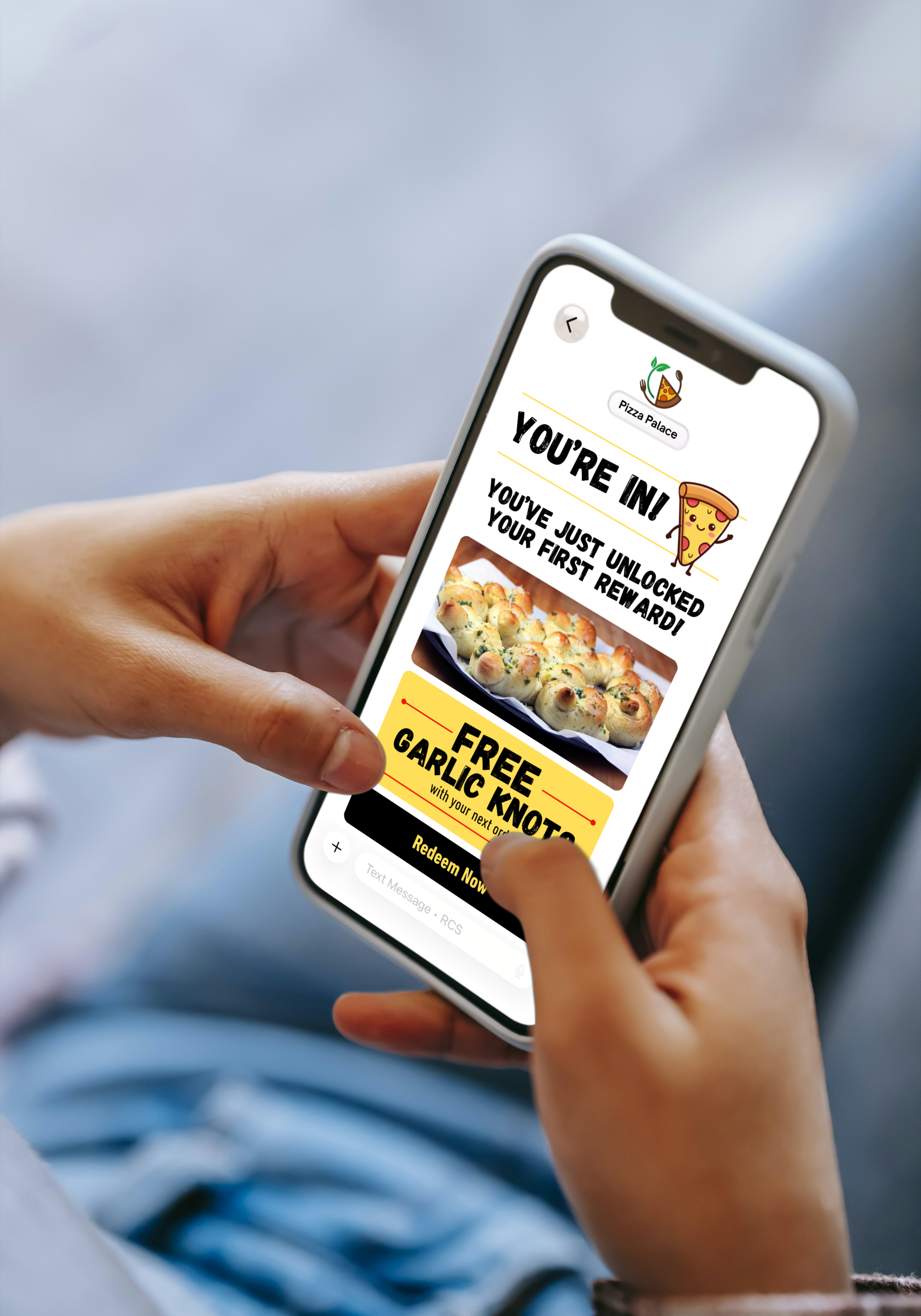 A person holds a smartphone displaying a reward notification from Pizza Palace, featuring a picture of bread rolls and a promotional offer for free garlic knots.