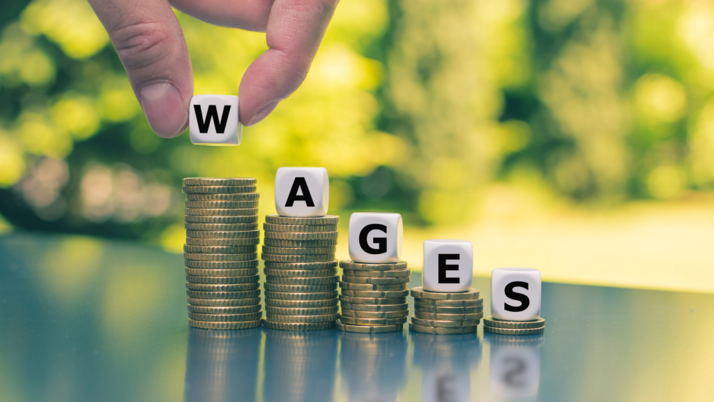 Wages displayed on stacked blocks with coins, illustrating wage and hour compliance requirements