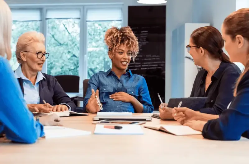 Several women seated around a table, actively participating in a group discussion.