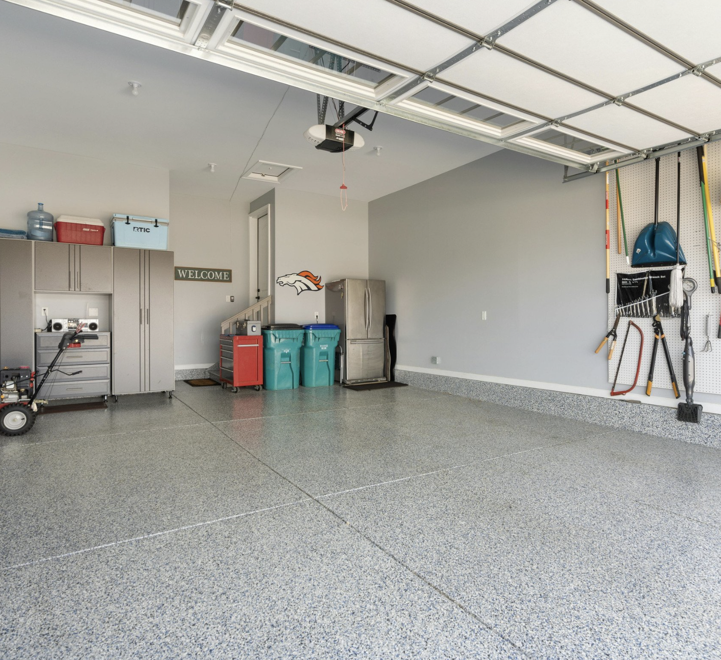 Empty residential garage with tools and storage cabinets on the left and wall-mounted yard equipment on the right.