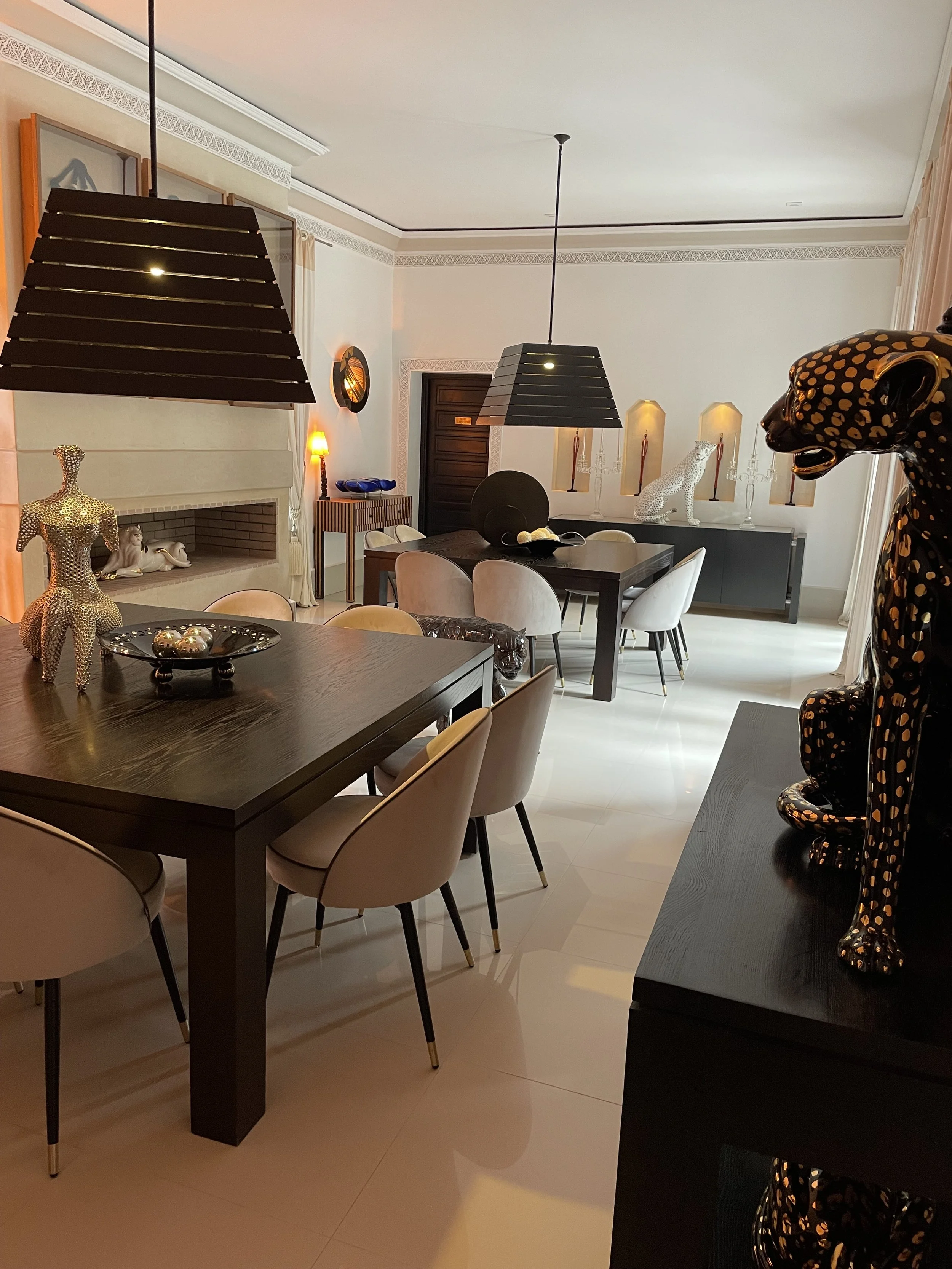 Salle à manger élégante avec un mobilier moderne, statues décoratives, et des luminaires suspendus.