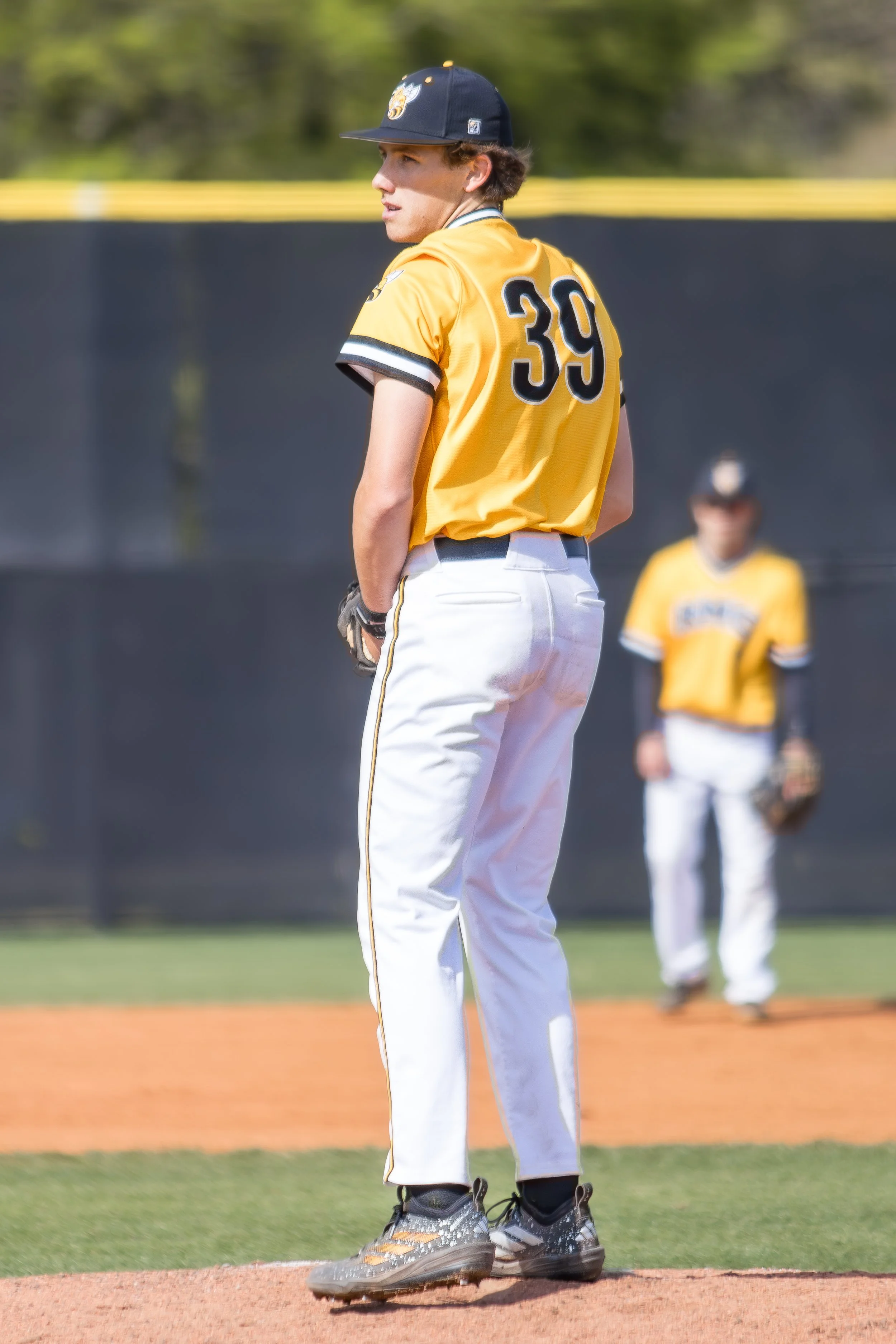 A baseball player standing on the pitcher's mound, wearing a yellow jersey with the number 39, white pants, and a navy blue cap. Another player is visible in the background.
