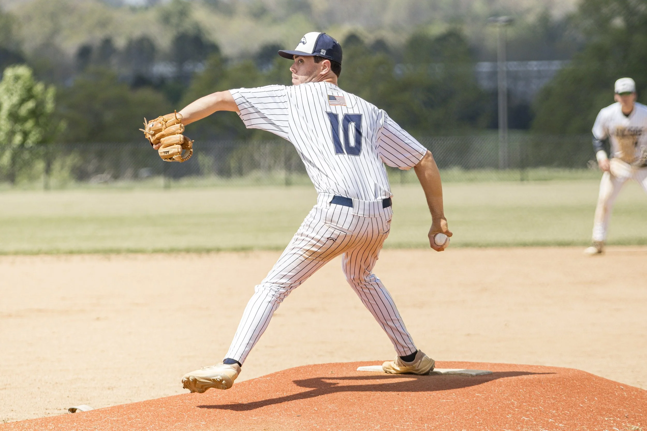 A baseball pitcher in a striped uniform throwing a pitch on a baseball field, with another player in the background.