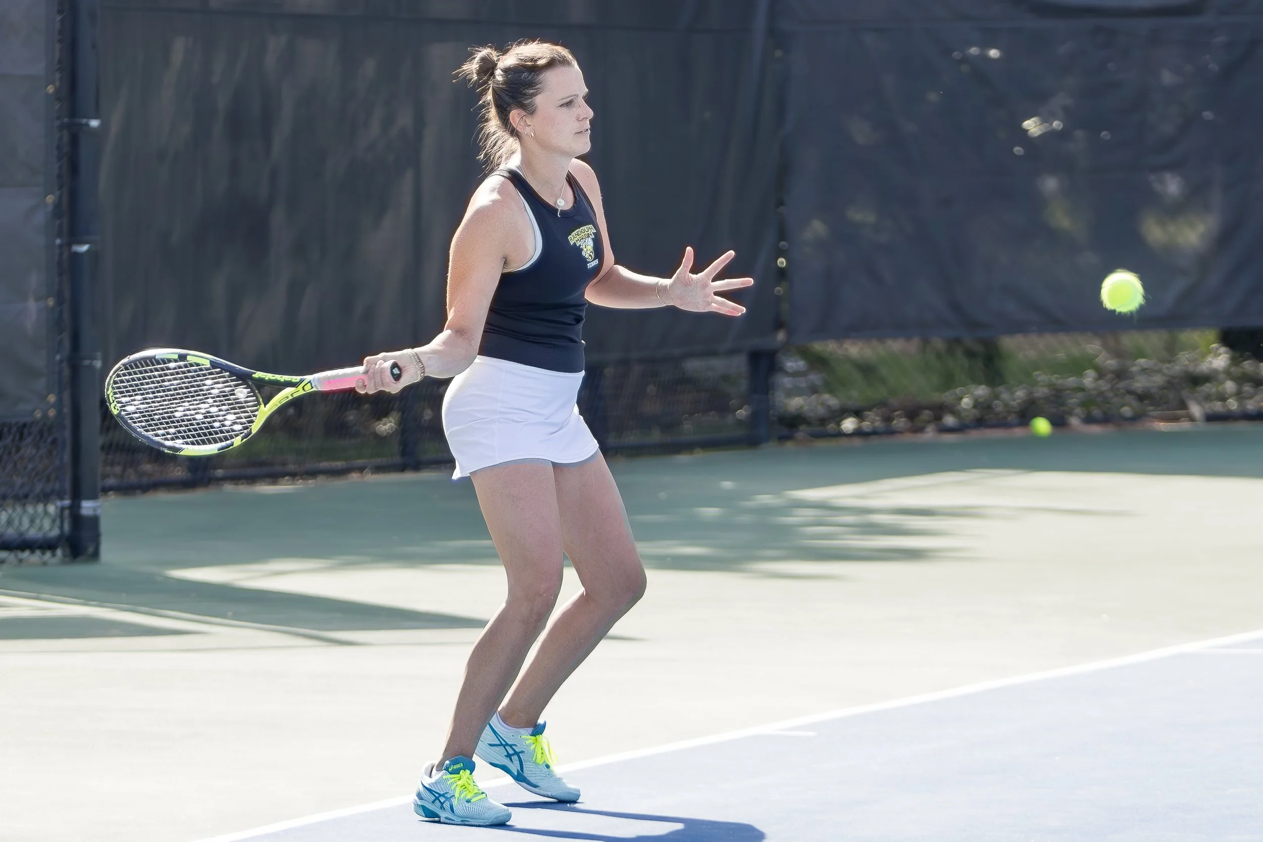 A woman playing tennis on an outdoor court, holding a tennis racket, preparing to hit a tennis ball.