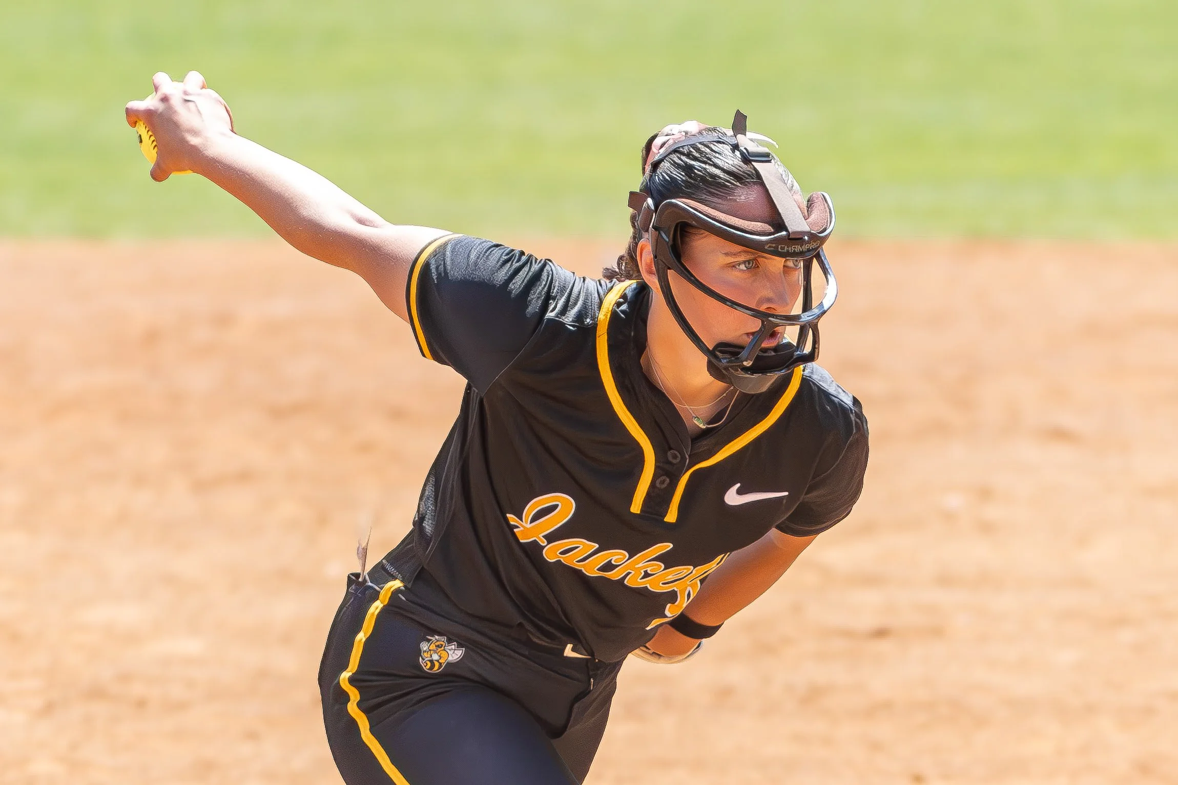 Female softball player in black and yellow uniform, running on a dirt field, wearing a face mask and goggles.