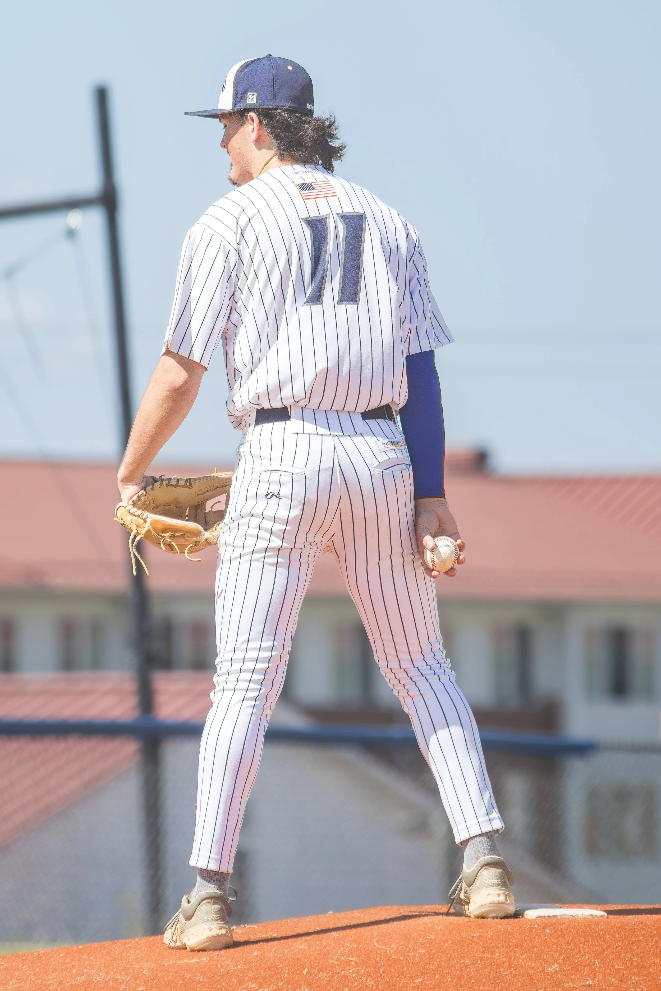 Baseball player in a pinstripe uniform holding a baseball on a mound, wearing a cap and glove, preparing to pitch.